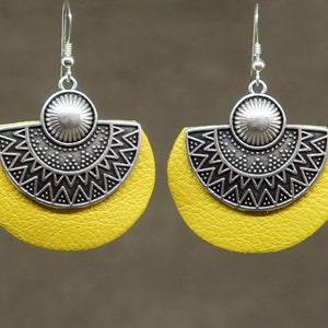 Könnte beinhalten: Ein Paar gelbe Lederohrringe mit silbernen geometrischen Designs. Die Ohrringe haben eine Halbmondform und verfügen über einen silbernen Kreis mit einer erhabenen Mitte.