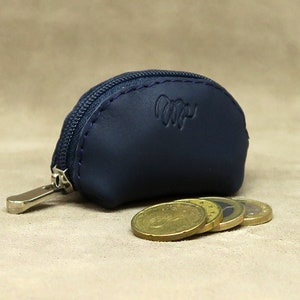 May include: A small, half-circle shaped, navy blue leather coin purse with a zipper closure. The purse has a silver zipper pull and the word "Wip" embossed on the front. Four gold coins are sitting in front of the purse.