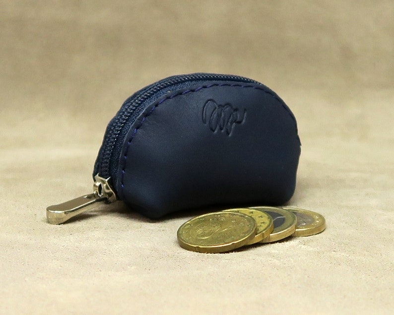 May include: A small, half-circle shaped, navy blue leather coin purse with a zipper closure. The purse has a silver zipper pull and the word "Wip" embossed on the front. Four gold coins are sitting in front of the purse.