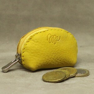 May include: A small yellow leather coin purse with a zipper closure. The purse has a small metal tag with the letters "MP" on it.