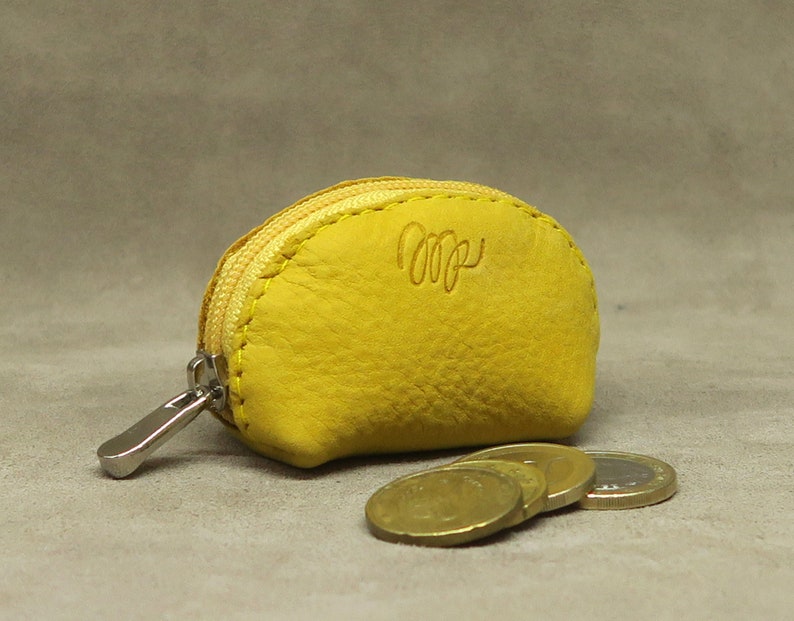 May include: A small yellow leather coin purse with a zipper closure. The purse has a small metal tag with the letters "MP" on it.