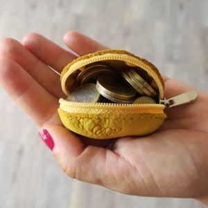 May include: A small yellow leather coin purse with a zipper closure, open to reveal a collection of euro coins.