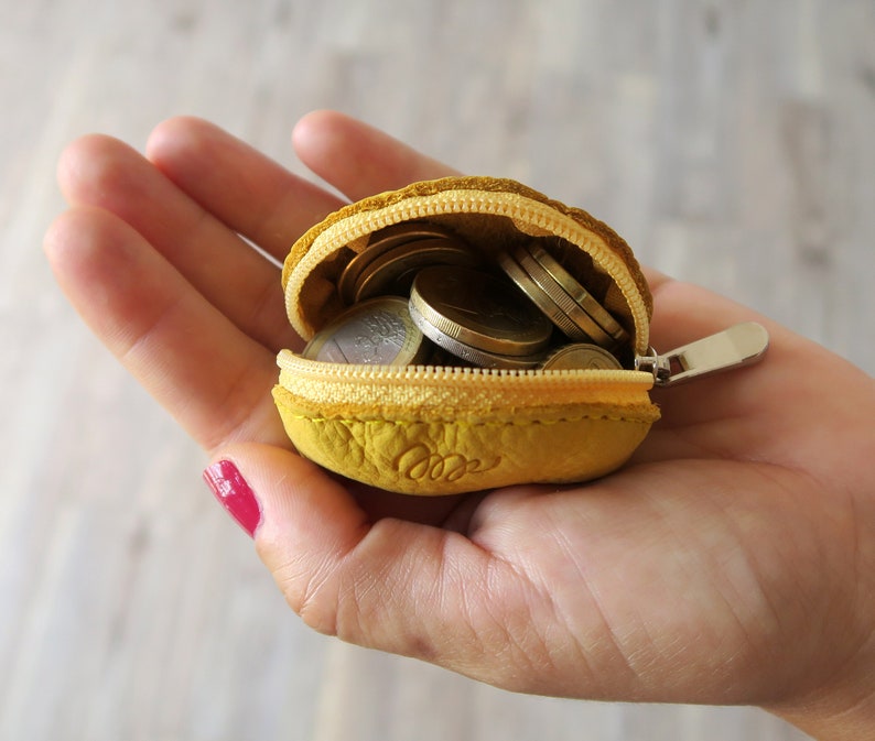 May include: A small yellow leather coin purse with a zipper closure, open to reveal a collection of euro coins.