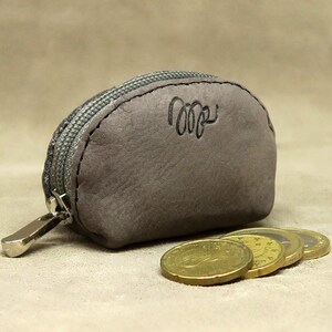 May include: A small, gray leather coin purse with a zipper closure. The purse has a silver zipper pull and the word "cozy" is embossed on the front.
