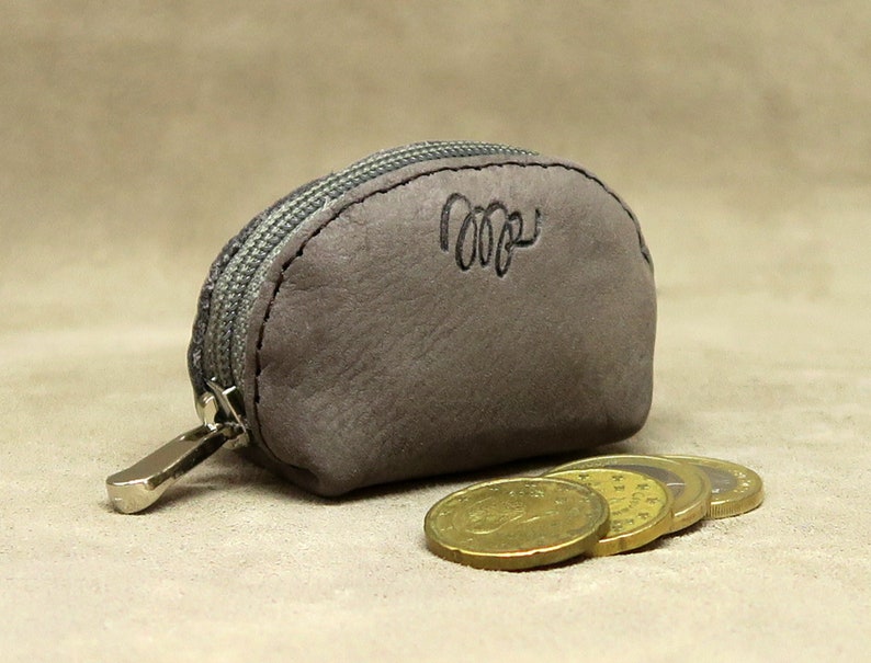 May include: A small, gray leather coin purse with a zipper closure. The purse has a silver zipper pull and the word "cozy" is embossed on the front.