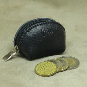 May include: A small black leather coin purse with a zipper closure and a silver zipper pull. The purse is sitting on a beige surface with four gold coins next to it.