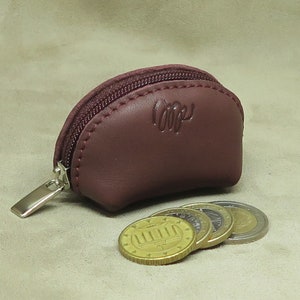 May include: A small, burgundy leather coin purse with a zipper closure. The purse is open and several gold coins are spilling out.