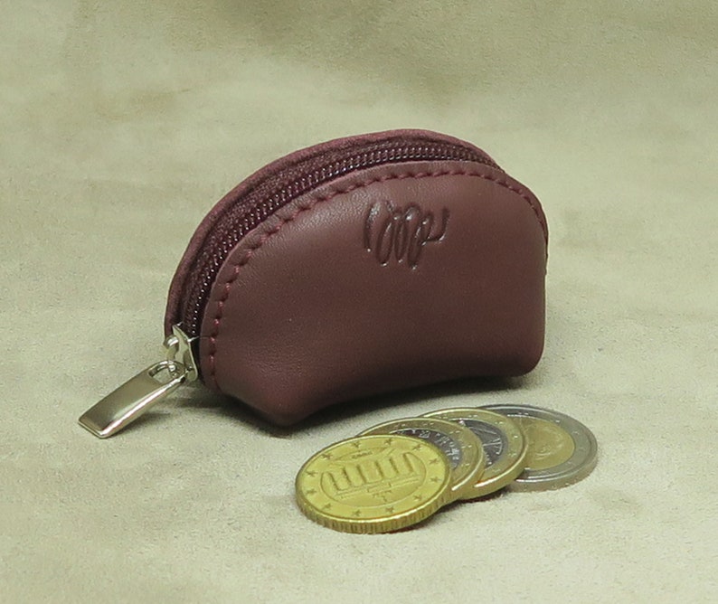 May include: A small, burgundy leather coin purse with a zipper closure. The purse is open and several gold coins are spilling out.
