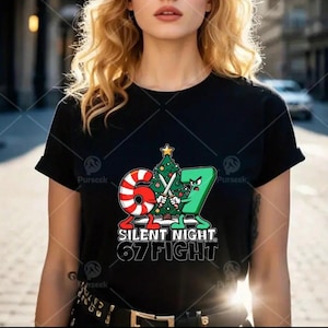 May include: Black t-shirt featuring a Christmas-themed graphic. The design includes a candy cane and the number 7, each holding swords and facing each other in front of a Christmas tree. The text "SILENT NIGHT 67 FIGHT" is below the figures.