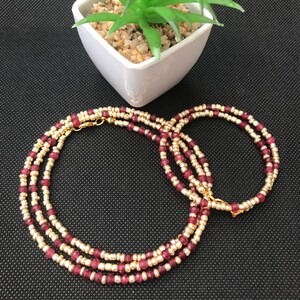 Puede incluir: Un brazalete de cuentas de tres hilos con cuentas doradas y burdeos. El brazalete está hecho de cuentas pequeñas y redondas y tiene un cierre dorado.