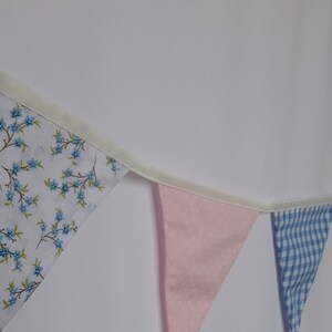 May include: A bunting with a white background and blue floral pattern, a pink bunting with white polka dots, a blue and white gingham bunting, and a white bunting with a pink floral pattern.