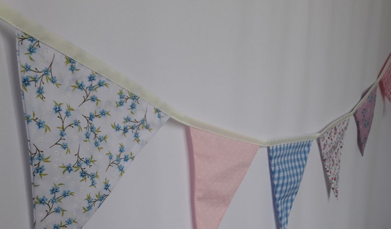 May include: A bunting with a white background and blue floral pattern, a pink bunting with white polka dots, a blue and white gingham bunting, and a white bunting with a pink floral pattern.