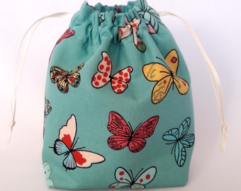 Op de afbeelding: Een turquoise trekkoordtas met een wit koord. De tas is versierd met een patroon van kleurrijke vlinders.