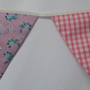 May include: A pink and white bunting with a floral pattern on one side and a gingham pattern on the other side.