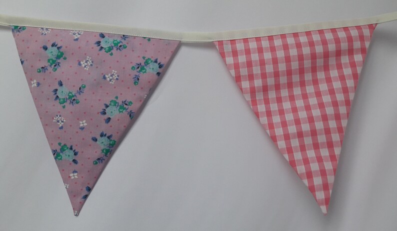 May include: A pink and white bunting with a floral pattern on one side and a gingham pattern on the other side.