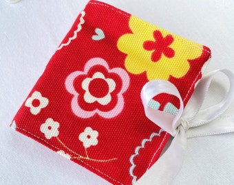 May include: A red fabric pouch with a white ribbon. The pouch has a floral pattern with pink, yellow, and white flowers.