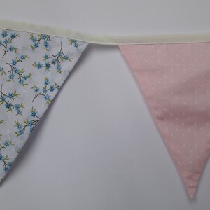 May include: A bunting with two triangular flags. One flag is white with a blue floral pattern and the other is pink with white polka dots.