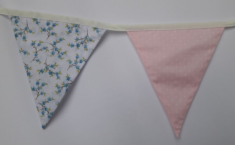 May include: A bunting with two triangular flags. One flag is white with a blue floral pattern and the other is pink with white polka dots.