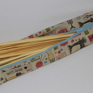 May include: A beige fabric zipped case with a blue zipper and a "with love" label. The case is filled with wooden knitting needles.