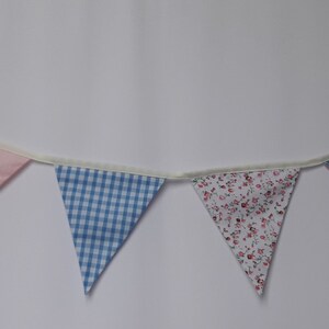 May include: A bunting banner with seven triangular flags. The flags are made of fabric and feature different patterns, including floral, gingham, and polka dots. The flags are connected by a white string.