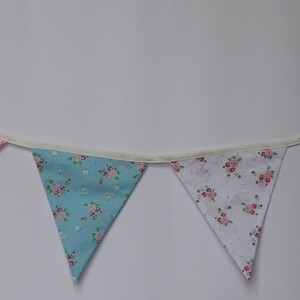May include: A bunting with six flags in a variety of patterns. The flags are made of fabric and have a white background with different colored patterns. The bunting is strung together with white string.
