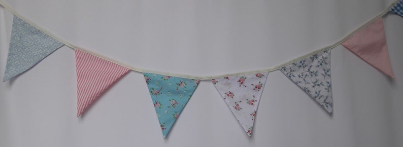 May include: A bunting with six flags in a variety of patterns. The flags are made of fabric and have a white background with different colored patterns. The bunting is strung together with white string.
