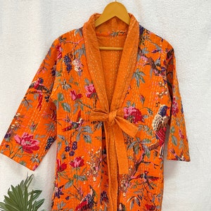 May include: A long orange quilted robe with a floral and bird print. The robe has a tie belt and a shawl collar.
