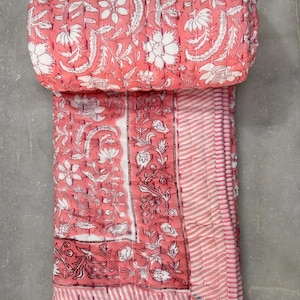 May include: A pink and white floral cotton quilt with a striped border. The quilt is folded in half and rolled up.