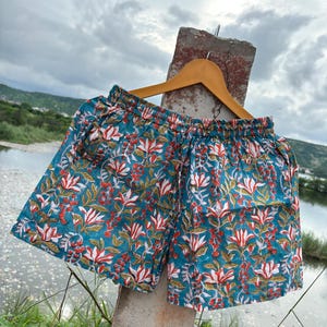 K&ouml;nnte beinhalten: T&uuml;rkise Baumwollshorts mit einem Blumendruck mit wei&szlig;en, roten und gr&uuml;nen Blumen. Die Shorts haben einen elastischen Bund und einen Kordelzug.