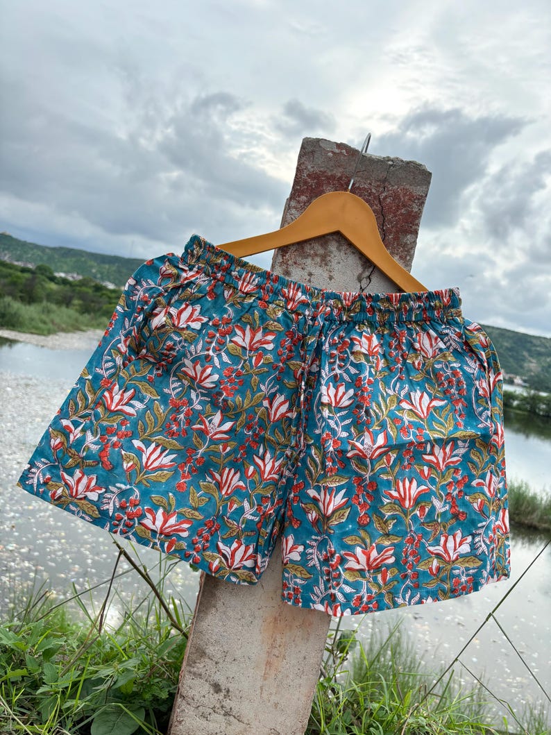 K&ouml;nnte beinhalten: T&uuml;rkise Baumwollshorts mit einem Blumendruck mit wei&szlig;en, roten und gr&uuml;nen Blumen. Die Shorts haben einen elastischen Bund und einen Kordelzug.