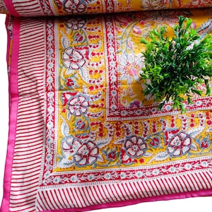 May include: Yellow and red floral patterned cotton fabric with a pink border. The fabric is folded in half and a small green plant is sitting on top of it.