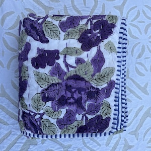 May include: A white cotton quilt with a purple floral pattern and a blue and white striped border.