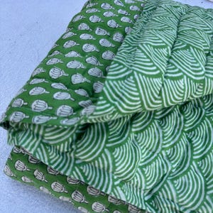 Könnte beinhalten: Eine grüne Baumwolldecke mit einem Blumenmuster auf der einen Seite und einem Wellenmuster auf der anderen Seite.