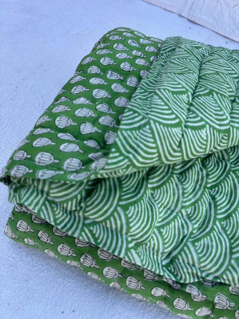 May include: A green cotton quilt with a floral pattern on one side and a wave pattern on the other side.