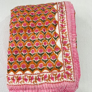 May include: A pink and orange floral patterned quilt with a white background. The quilt has a pink and white striped border.