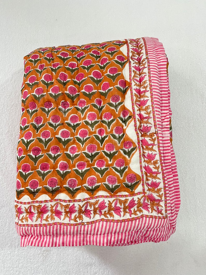 May include: A pink and orange floral patterned quilt with a white background. The quilt has a pink and white striped border.