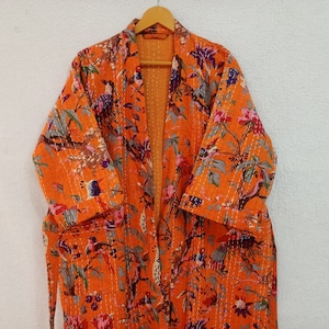 Może przedstawiać: Pomarańczowa szlafrokowa tunika z bawełny z nadrukiem kwiatowym i ptaków. Tunika ma pasek do wiązania i długie rękawy.