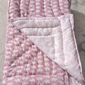 May include: A pink and white reversible baby quilt with a pattern of elephants on one side and a floral pattern on the other side.