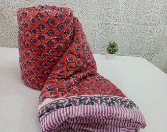 May include: A red and purple floral print cotton quilt with a white and purple striped border. The quilt is rolled up and sitting on a white surface.