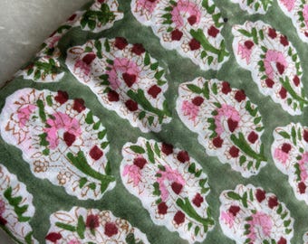 May include: Green fabric with a repeating floral pattern. The design features white paisley shapes filled with pink flowers and maroon accents, set against a green background. The fabric appears to be folded.