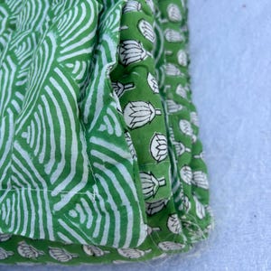 May include: Close-up of a green fabric with a white pattern. The fabric is folded over itself, showing the different patterns on each side. The fabric is made of cotton and has a soft, natural feel.
