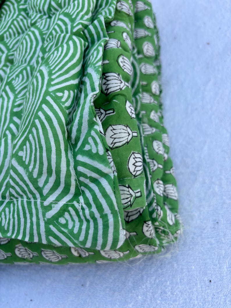 May include: Close-up of a green fabric with a white pattern. The fabric is folded over itself, showing the different patterns on each side. The fabric is made of cotton and has a soft, natural feel.