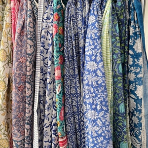 May include: A collection of ten colorful scarves with floral patterns in shades of blue, green, pink, and white. The scarves are hanging on a rack.