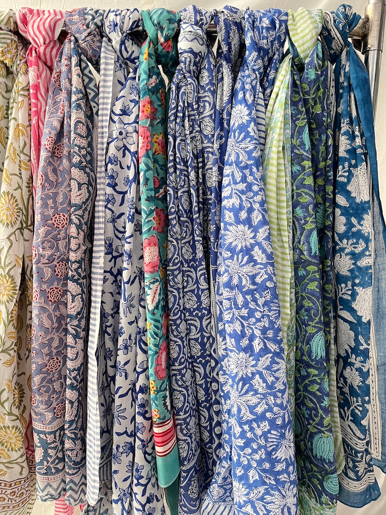 May include: A collection of ten colorful scarves with floral patterns in shades of blue, green, pink, and white. The scarves are hanging on a rack.
