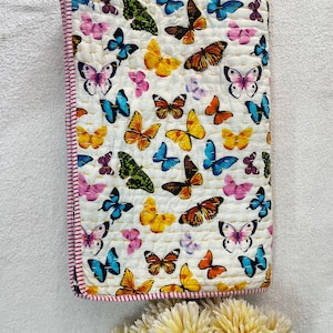May include: A white cotton quilt with a colorful butterfly pattern. The quilt has a pink and white border.