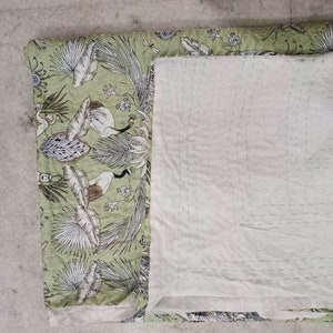 May include: A green and white kantha quilt with a floral pattern. The quilt is folded in half and has a white backing.