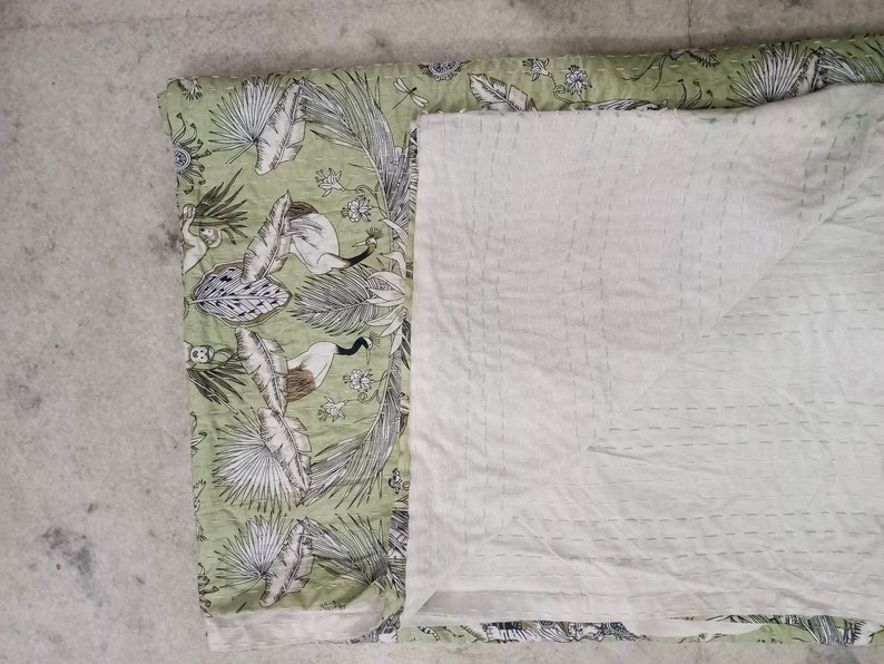 May include: A green and white kantha quilt with a floral pattern. The quilt is folded in half and has a white backing.