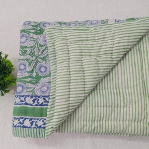May include: A green and white striped cotton quilt with a floral print on one side. The quilt is folded in half and the floral side is facing up.