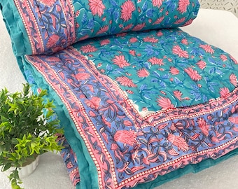 May include: A teal blue and pink floral patterned quilt with a white background. The quilt is folded in half and has a border of pink and blue floral designs.