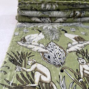 May include: A green kantha quilt with a white and brown floral pattern featuring monkeys and birds. The quilt is made of cotton and is hand-stitched.